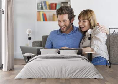 Happy successful young couple with laptop on sofa in modern apartment Wall mural