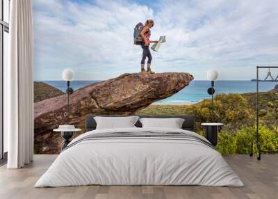 Hiker on a rock precipice holding a map Wall mural