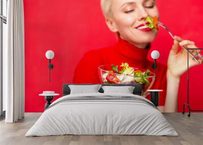 Beautiful caucasian woman eating salad over red background Wall mural