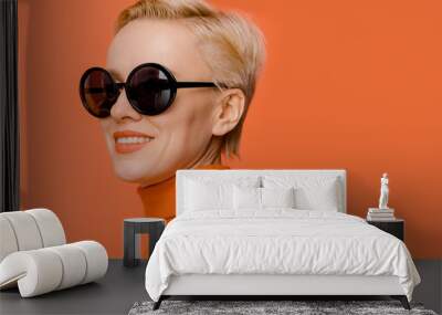 Beauty portrait of female model wearing trendy sunglasses over orange background Wall mural