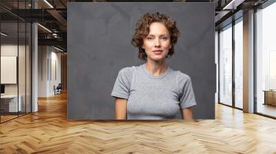 portrait of a serious brunette woman with curly hair wearing casual attire over grey background Wall mural