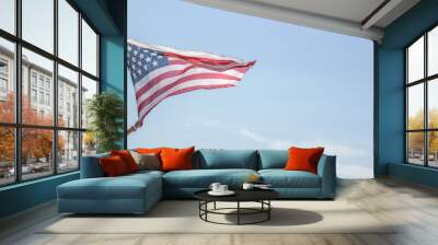 Young woman waving with american flag against blue sky Wall mural