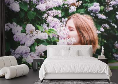 Pretty ginger girl enjoying the aroma of the blooming lilac flowers. Wall mural