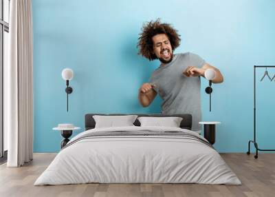 a curly-headed handsome man wearing a gray t-shirt is standing with a cheerful smile and dancing wit Wall mural