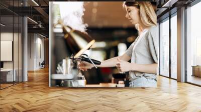 A good looking slim blonde with long hair,dressed in casual outfit,is cooking coffee in a modern coffee shop. Process of making coffee is shown. Wall mural