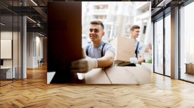 A young handsome smiling mover wearing uniform is reaching for t Wall mural