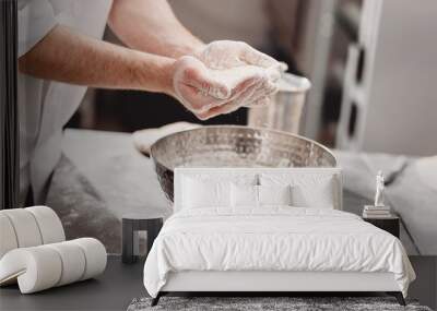 Baker adds flour to dough in an iron bowl on the table in the bakery Wall mural