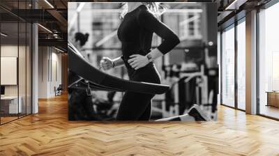 Black and white photo of the athletic girl dressed in a black sportswear running on the treadmill in the modern gym Wall mural