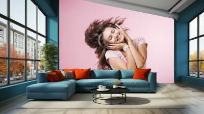 Brown-haired girl with headphones listening to music with closed eyes on pink background Wall mural