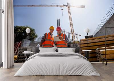 civil architect and construction manager dressed in orange work vests and helmets discuss a building Wall mural