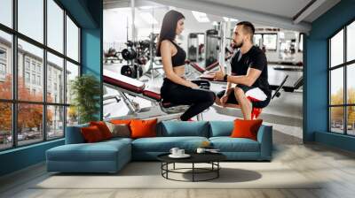 Coach talks with athletic girl dressed in black sport clothes sitting on the bench in the gym Wall mural