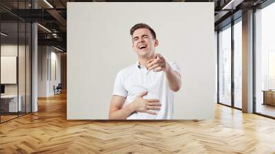 Guy dressed in a white t-shirt and jeans laughs and keeps hand on the belly on a white background in the studio Wall mural