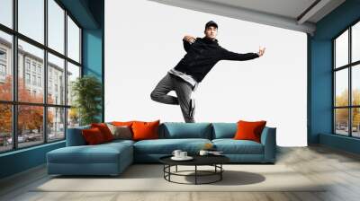 Handsome young man wearing a black sweatshirt, gray pants and a cap dancing street dances on a white background Wall mural