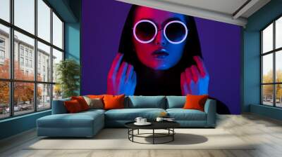 Portrait of fashion young girl in a black sweater with a hood and round sunglasses in red and blue neon light in the studio Wall mural