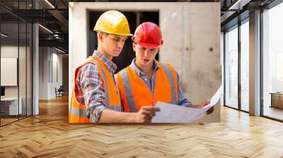 Structural engineer and construction manager dressed in work clothes and hard bats explore construction documentation on the building site Wall mural