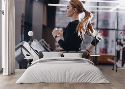 The athletic girl dressed in a black sportswear running on the treadmill in the modern gym Wall mural