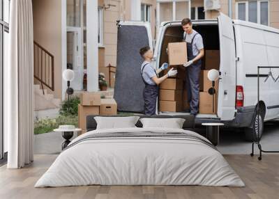 Two young handsome movers wearing uniforms are unloading the van full of boxes. House move, mover service. Wall mural