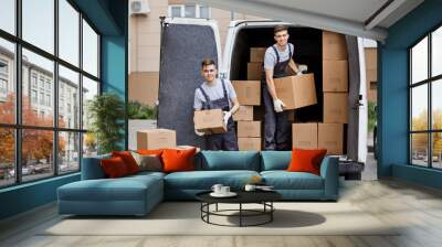 Two young handsome smiling movers wearing uniforms are unloading the van full of boxes. House move, mover service. Wall mural