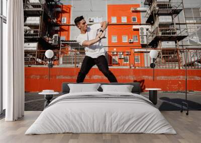 Young guy dressed in jeans and t-shirt is dancing modern dance in the street on the background of urban buildings in the warm day Wall mural