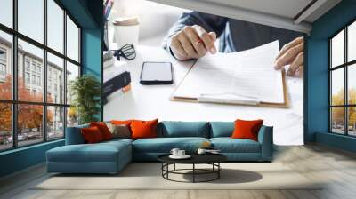 A man work at home holding pen checking financial reports and business contract from documents before sign to make new business SME. Wall mural