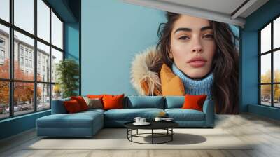 A beautiful Mexican woman model poses in a winter coat against a blue background, with space for text Wall mural