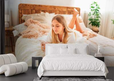 Young beautiful girl having relaxed morning in bed with her mobile phone Wall mural