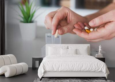 Female elderly hands sorting pills. Closeup of medical pill box with doses of tablets for daily take a medicine with white, yellow drugs and capsules. Young woman getting her daily vitamins at home.  Wall mural