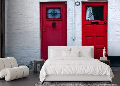 Two red wooden front doors in the white brick wall. Two vintage red doors with window at the top. Wall mural