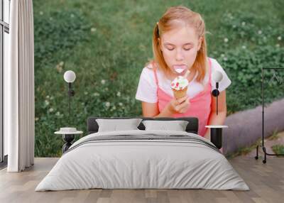 Teenage girl in summer dress sitting on the grass eating ice cream Wall mural