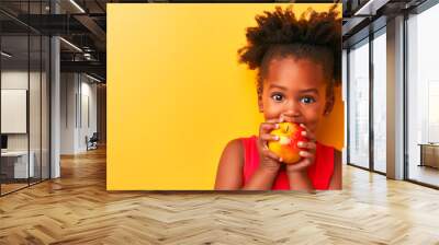 cheerful little African American girl in a red dress eating an apple on a bright yellow background copy space healthy vegetarian food for children Wall mural