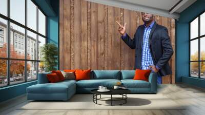 African black man with beard pointing away side with finger on wood background, copyspace. He smiling and looking at camera. Wall mural