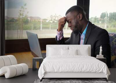 Afro american businessman tries to type on computer sitting in cafe. Black man works on laptop but it's broken and he is nervous and knocking on the keys. He has a computer problems. Battery is low. Wall mural