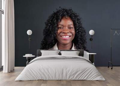 Attractive young African-American woman with curly hair smiles and laughs looking into camera on black background in studio close view Wall mural