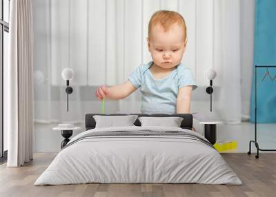 Baby girl plays around with xylophone toy on floor in house. Small child in ordinary clothes learning to play music using colorful toys Wall mural