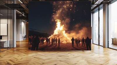 Crowd of people stands around majestic bonfire reaching dark sky at night. Celebration of old holiday by whole village. Lighting fire for rituals, close-up Wall mural