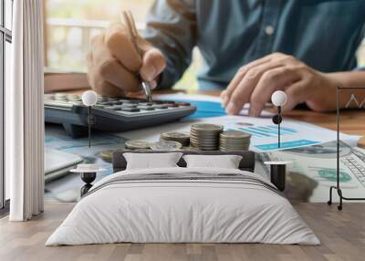 Person calculating finances with coins, calculator, and financial documents on desk. Wall mural