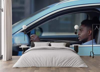 Serious African American driver sits in car cabin in a traffic jam, holding the steering wheel. Wall mural