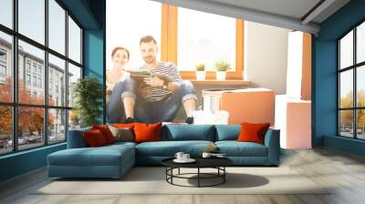 Attractive couple sitting on home floor looking at jurnal and smiling at each other. Wall mural