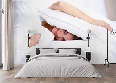 Female lying on bed and closing her ears with pillow Wall mural