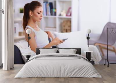 Portrait of young woman watching TV at home sittin on sofa Wall mural