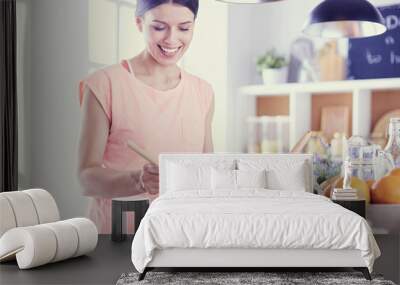 Smiling young woman mixing fresh salad in the kitchen. Wall mural