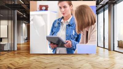 Two young woman standing near desk with instruments, plan and laptop. Wall mural