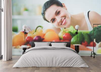 Young and cute woman sitting at the table full of fruits and vegetables in the wooden interior Wall mural