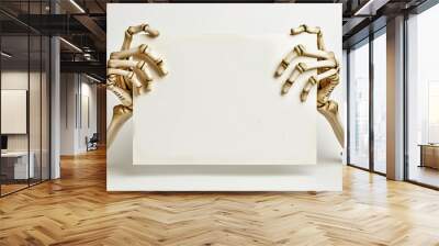 Skeleton hands holding blank white sign against white background. Pair of skeleton hands holds empty white sheet of paper, positioned prominently against plain background, Halloween template. Wall mural