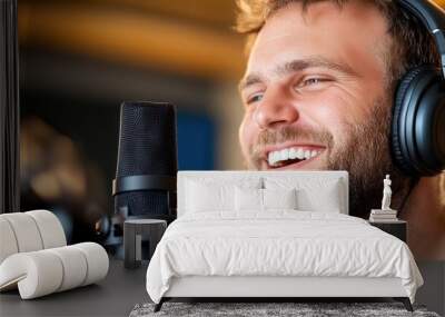 A cheerful man wearing headphones smiles widely while seated by a studio microphone, representing joy and enthusiasm in the musical and recording experience. Wall mural