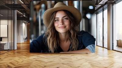 A cheerful woman wearing a hat, smiling in an industrial background, embodying a sense of freedom, adventure, and modern rustic charm. Wall mural