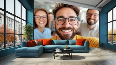 A group of friends takes a cheerful selfie in a modern office setting, showcasing a happy workplace environment with natural lighting and casual attire. Wall mural