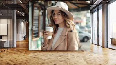 A smiling woman in a trendy outfit holds a coffee cup on a city street, exuding confidence and style Wall mural