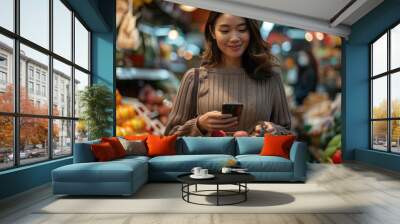 A woman holding a basket filled with fresh fruits checks her phone while shopping in a grocery store, highlighting the everyday life and modern shopping adventures. Wall mural