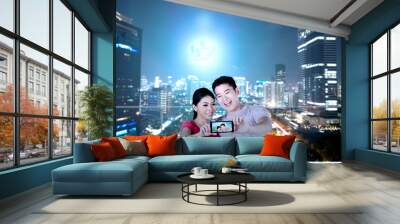 Asian couples making a selfie using a camera phone with skyscrapers  background Wall mural